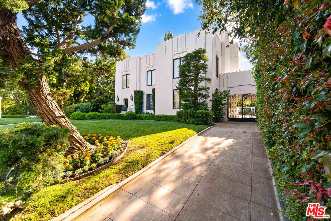 The white Art Deco facade of the Smith House under a clear blue Los Angeles sky, framed by mature topiary.