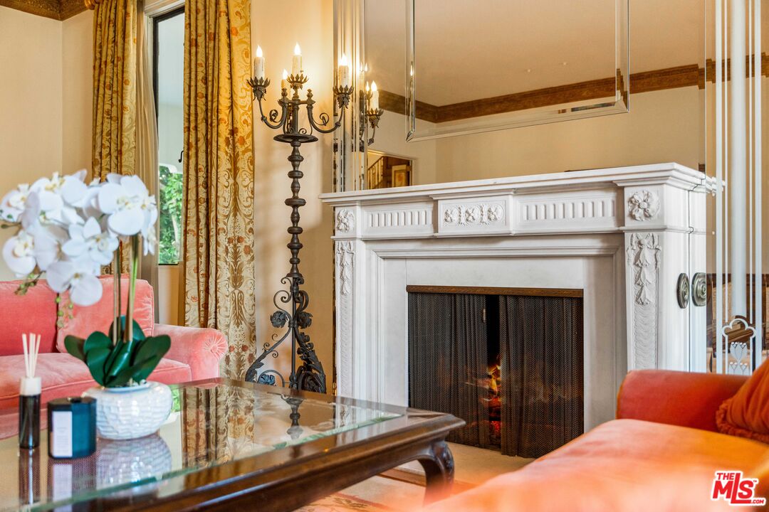 Living room with carved white marble fireplace lit, beveled mirror panels, and Art Deco candelabra.