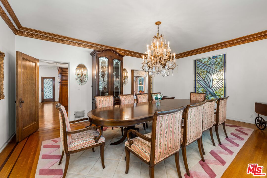 Formal dining room with crystal chandelier, gilded crown molding, and an original stained-glass panel.