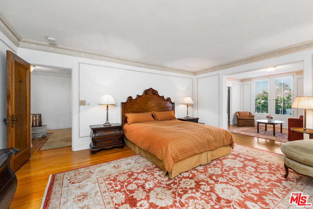 The primary bedroom suite with a carved wood headboard, oak floors, and a sitting alcove in afternoon light.