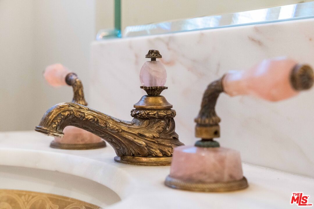 Vintage gilded brass sink fixtures with rose-quartz handles set against Calacatta marble.
